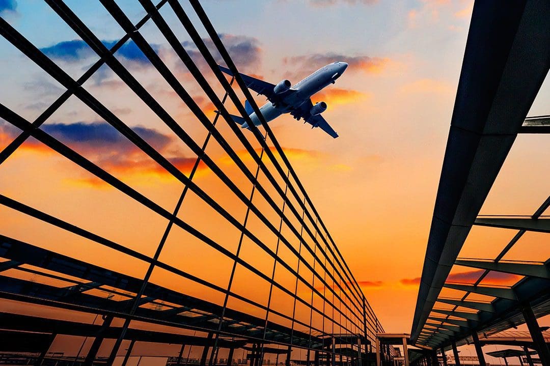 Airplane flying over airport at sunset.